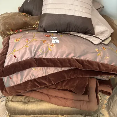 Stack of bedding and decorative throw pillows featuring floral embroidery and velvet trim.