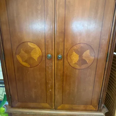 Traditional wooden armoire featuring double cabinet doors with circular marquetry inlay above two bottom drawers with brass pulls.