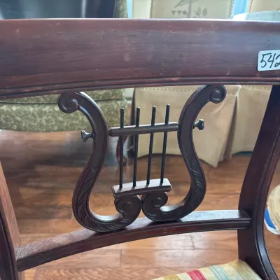 Close-up of a mahogany Duncan Phyfe style chair back, featuring a carved lyre slat detail with metal strings.