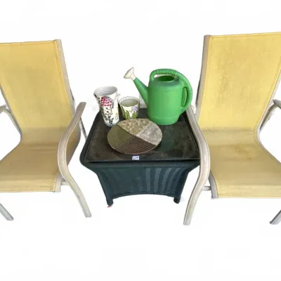 Pair of outdoor yellow sling armchairs flanking a dark wicker side table with glass top, set with garden decor including a green plastic...