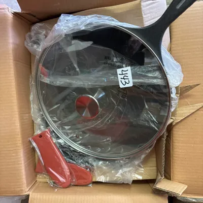 Cast iron skillet set with glass lid and red silicone handle covers, packed in a cardboard box.