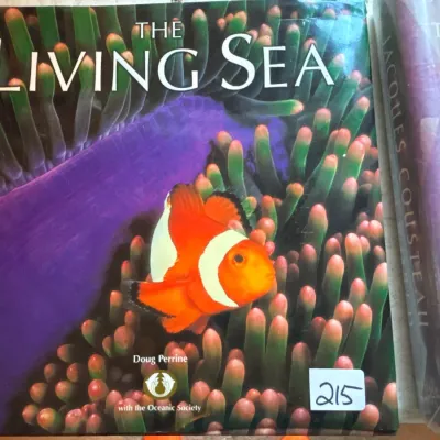 Hardcover copy of "The Living Sea" by Doug Perrine with the Oceanic Society, featuring a vibrant clownfish photo cover.