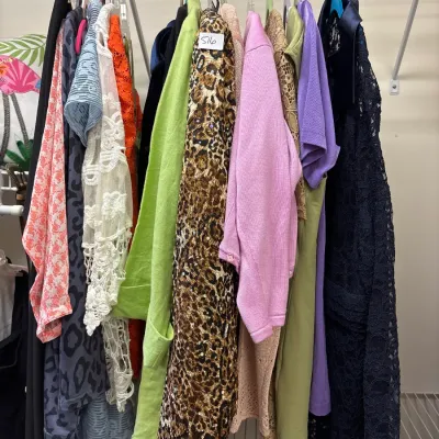 Collection of women's vintage and contemporary clothing hanging on a wire closet rack, including a sequined leopard print coat, pink...