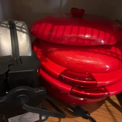 Rotating waffle maker alongside a stacked red electric countertop appliance stored on a cabinet shelf.