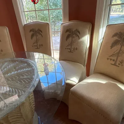 Set of four tropical-style dining chairs with palm tree motif embroidery, paired with a carved palm-frond motif glass-top table.