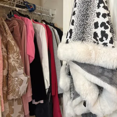Closet filled with assorted women's outerwear and tops, featuring a faux fur-trimmed patterned poncho hanging on the door.