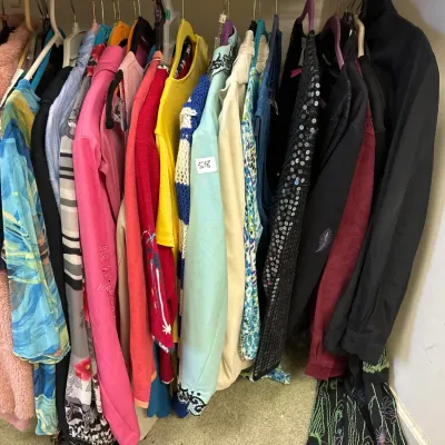 A rack of colorful women's clothing, featuring a pink fleece coat, patterned tops, sweaters, and a sequined cardigan.