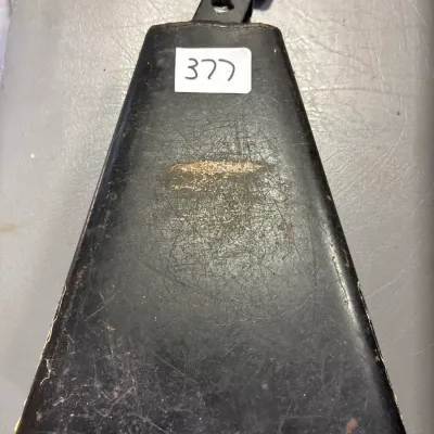 Black metal percussion cowbell with mounting bracket and wing screw, showing heavy surface wear and scratching.