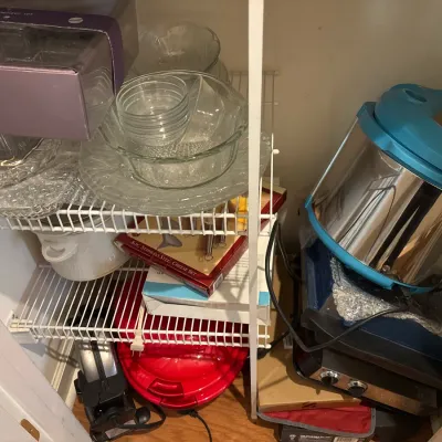 Pantry closet filled with kitchenware, including a stainless steel electric pressure cooker, glass mixing bowls, and small kitchen...