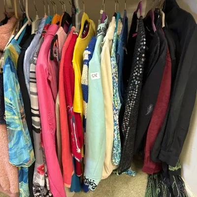 Closet rack packed with an assortment of women's vintage and contemporary clothing, featuring a pink faux fur coat, sequined top,...