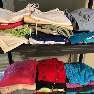 Selection of folded women's clothing, including pants and embellished tops, stacked on black plastic shelving units.
