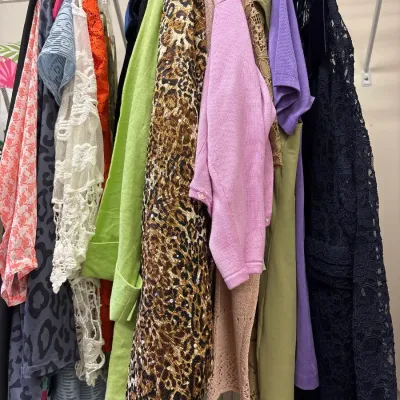 Selection of women's vintage and contemporary clothing hanging on a wire closet rack, including patterned blouses, a sequined...
