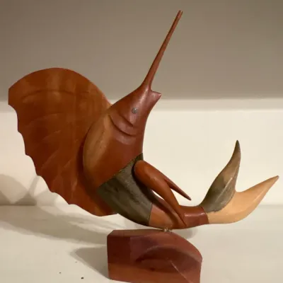 Hand-carved wooden sailfish sculpture mounted on a wooden base, featuring multi-tone wood grain details.