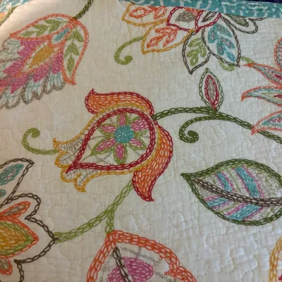 Folded quilted blanket featuring colorful embroidered floral and paisley patterns on a white background.