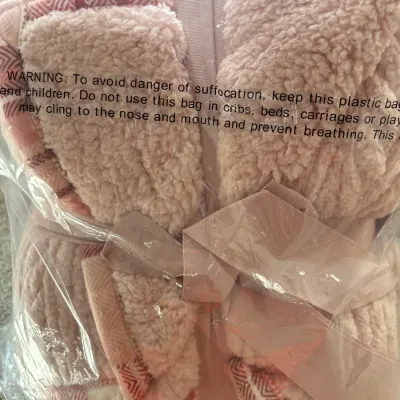 Plush pink fleece sherpa blanket set tied with a bow and sealed in original plastic packaging.
