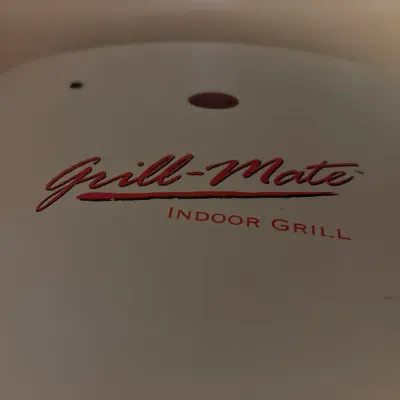 Close-up of a Grill-Mate indoor electric grill featuring a white exterior with red branding.
