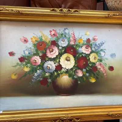 Framed floral still life oil painting depicting a colorful bouquet in a spherical vase, presented in an ornate gilt wood frame.