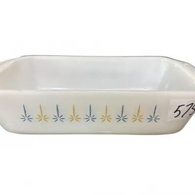 Vintage Anchor Hocking Fire-King milk glass loaf pan featuring a mid-century atomic starburst motif in blue and yellow.