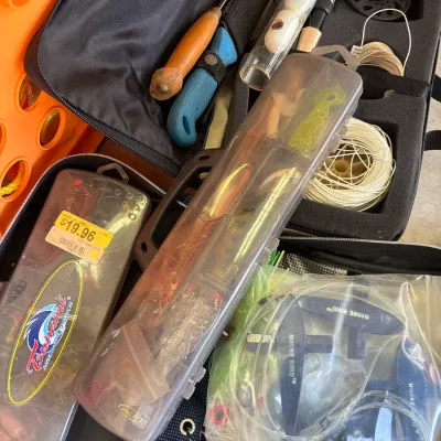 Collection of fishing gear including tackle boxes, lures, a fly reel with extra line, knives, and Boone Bird teasers.