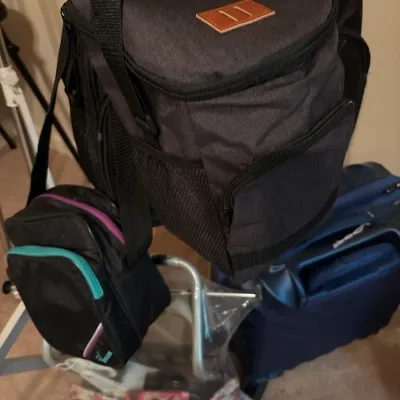 Collection of soft-sided travel bags and small luggage items, including a charcoal grey insulated cooler bag and a black shoulder bag.