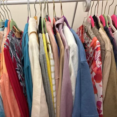 A rack packed with women's colorful vintage and contemporary clothing hanging on metal and plastic hangers.