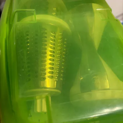 Lime green plastic manual food slicer and spiralizer set with metal drum attachments inside a fitted storage case.