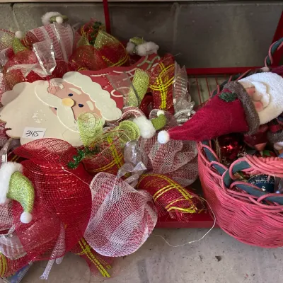 Festive Christmas decorations including a large deco mesh Santa wreath paired with a red wicker basket filled with ornaments and a plush...