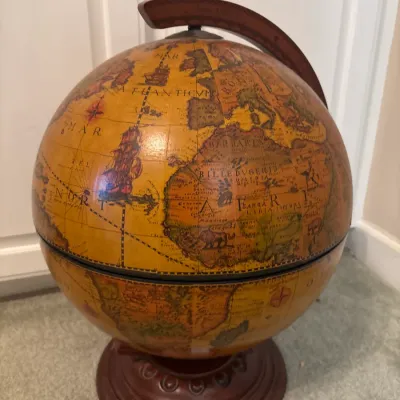 Vintage-style tabletop globe bar featuring an antique map graphic, hinged opening, and decorative wooden meridian and stand.