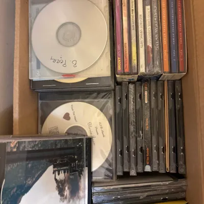 Cardboard box filled with assorted compact discs, including commercial music albums, holiday collections, and home-burned CD-Rs.