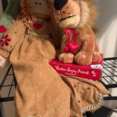 Handcrafted fabric rag doll in a embroidered brown dress displayed alongside a plush Valentine Singing Animal lion sitting on its...