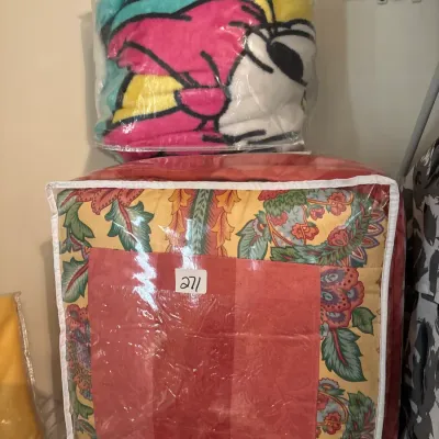 Two packaged bedding items, including a colorful vintage-style floral comforter and a bright plush character blanket in zippered plastic...