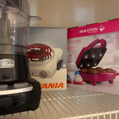 Wolfgang Puck Bistro Collection food processor alongside boxed small appliances, including a single-burner hot plate and a Holstein...