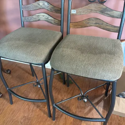 Pair of contemporary counter-height bar stools with black metal frames, wooden slat backs, and beige upholstered cushion seats.