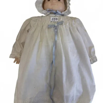 Vintage antique-style porcelain or bisque baby doll dressed in a long white christening gown with lace trim, a matching lace bonnet, and...