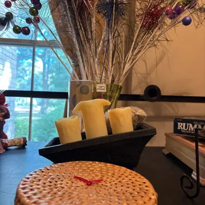 Set of three flameless pillar candles in a black decorative trough tray, accompanied by a round woven storage basket with a red handle...