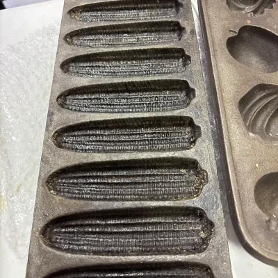 Vintage cast iron cornbread pans, including an eight-slot corn cob shaped mold and a autumn-themed fruit and leaf shape mold.