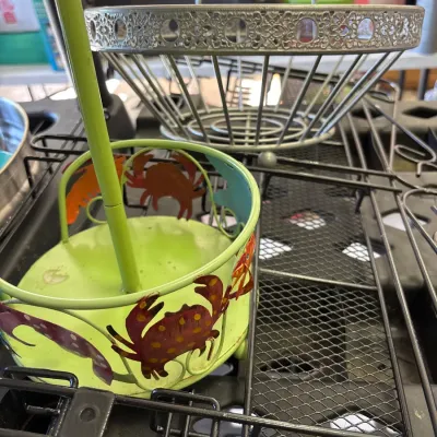Lime green metal paper towel holder with cut-out crab details, shown next to a wire fruit basket.
