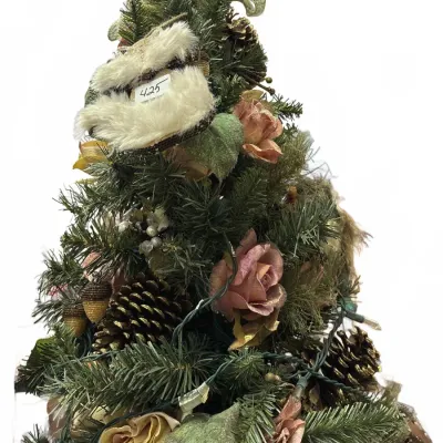 Decorated tabletop artificial Christmas tree with pink and yellow faux roses, pinecones, strings of lights, and a fur-trimmed topper.