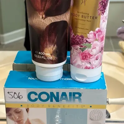 Tubes of Korres Vanilla Chestnut and Nakery Beauty Enchanted Lilac body butter sitting atop a boxed Conair Body Benefits touch massager.