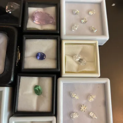 Collection of loose gemstones, including diamonds and various colored stones, displayed in individual gemstone display cases.