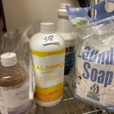 Collection of assorted household cleaning products, including Real Simple wrinkle release treatment and a bag of laundry soap.