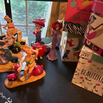 Collection of humorous novelty figurines featuring women riding scooters, alongside Red Hat Society figurines and patterned gift boxes.