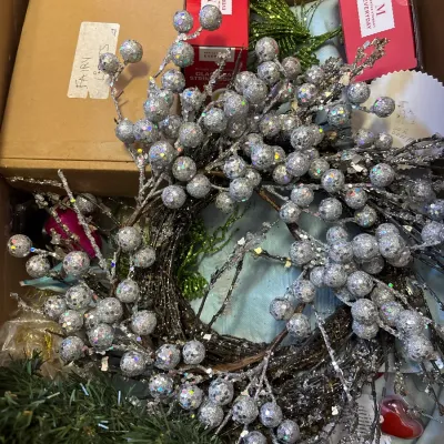 Box of holiday decor items, including a silver glitter berry wreath, boxed Martha Stewart string lights, and artificial greenery.
