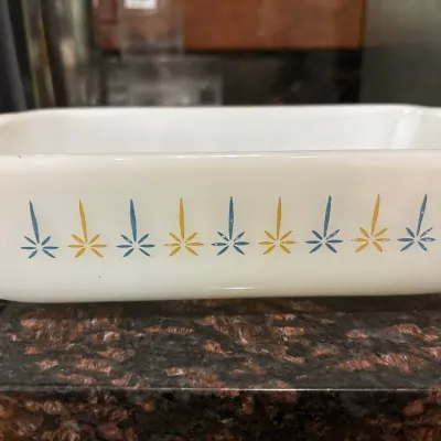 Vintage white Pyrex glass baking dish featuring a mid-century atomic starburst pattern in blue and yellow.