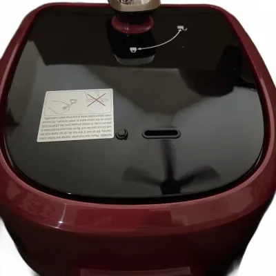 Modern burgundy and black electric pressure cooker lid, showing safety release valve and warning label.