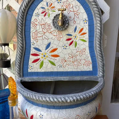 Wall-mounted decorative water fountain with a faux mosaic floral pattern, brass spigot, and rope-trim border.