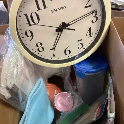 Sharp quartz round wall clock with a cream frame sitting in a box of assorted household kitchen items.