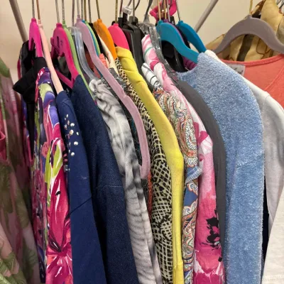 Selection of women's colorful tops, sweaters, and blouses hanging on a metal clothing rack.