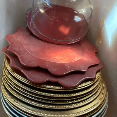 Stack of decorative charger plates in silver, beaded gold, and scalloped red designs, topped with a glass dome server.
