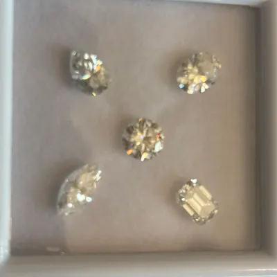 Set of five loose faceted gemstones in various shapes including round, oval, marquise, pear, and emerald cut, displayed in a white...